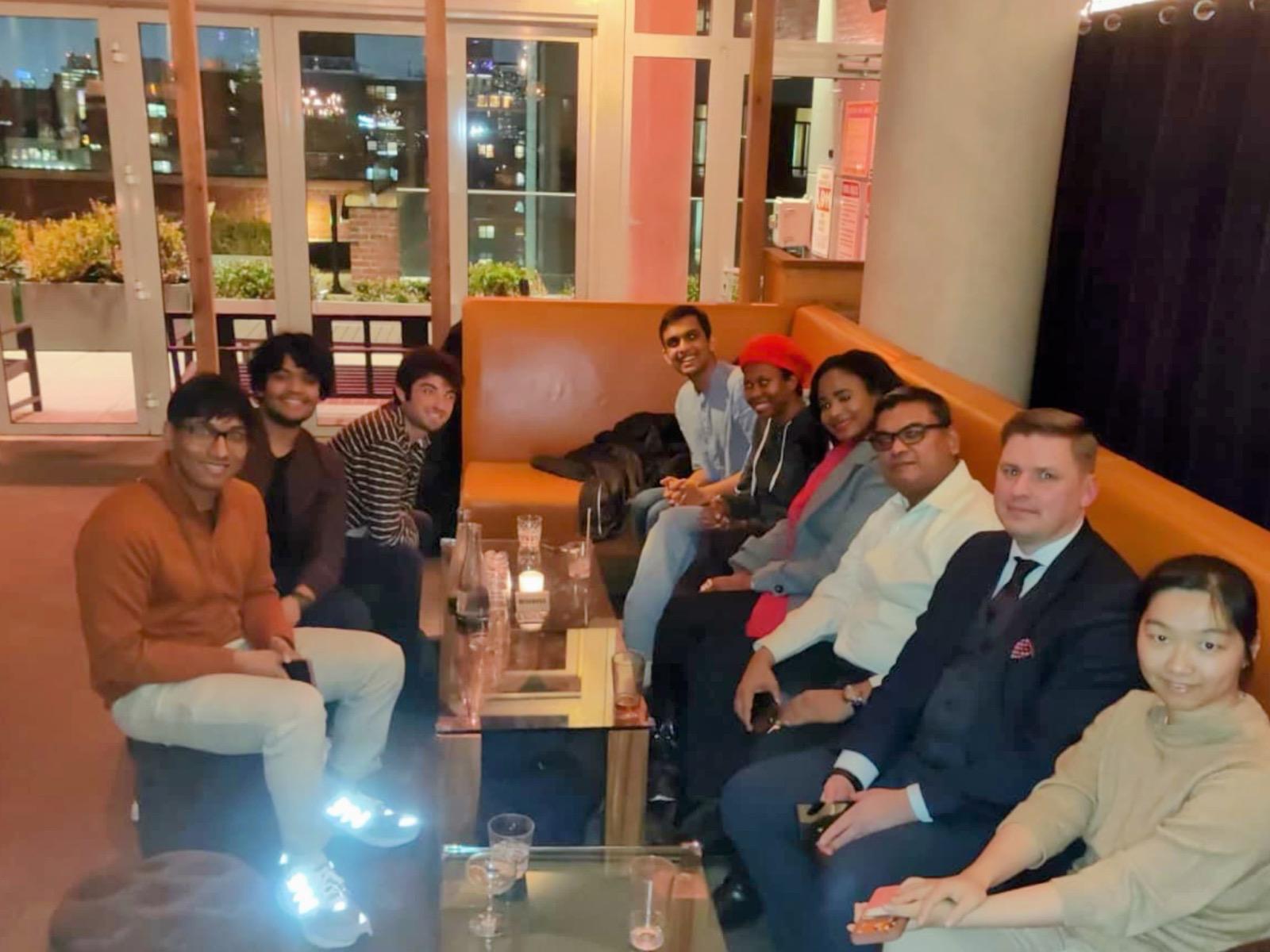 Group photo of the eChai Founders Mixer at Mr Purple in Manhattan: nine founders and operators on the rooftop lounge couches with the New York skyline through the windows behind them