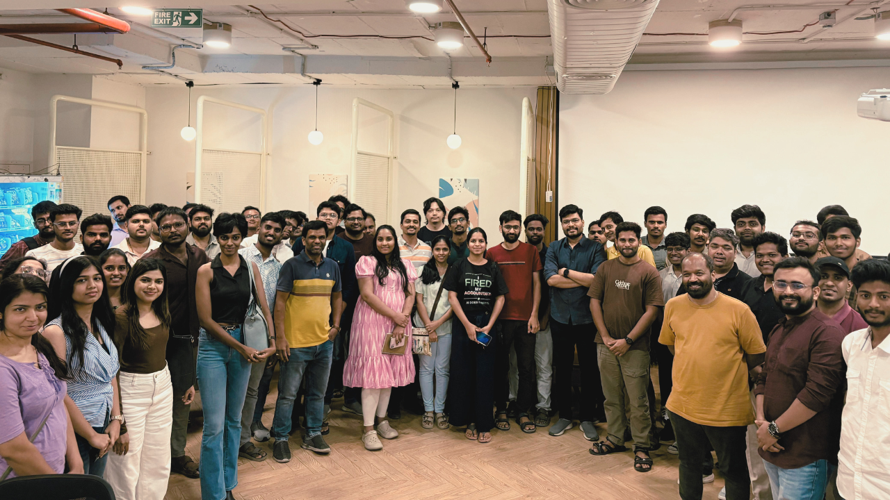 Group photo at an eChai Ventures and Petpooja AI Enablement for SMEs and Startups session: founders, operators, and SME leaders standing together in a packed indoor venue under warm pendant lights, with 'Fire Exit' signage on the back wall