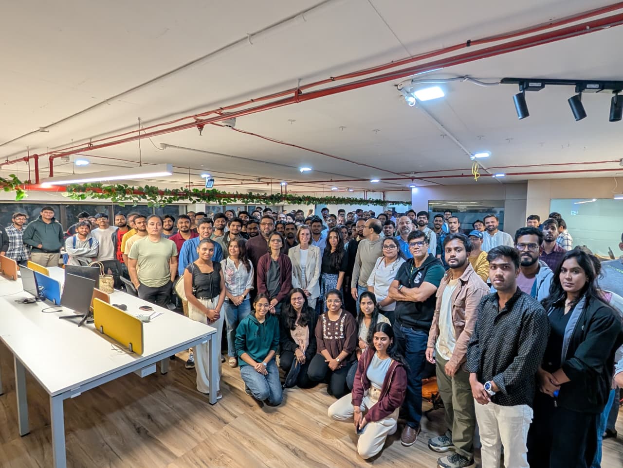 Wide group photo at an eChai Pune meetup: 80+ early-stage founders standing together in a coworking floor with desks on the left and exposed industrial ceiling overhead